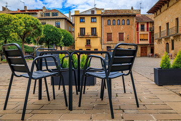 Table and chairs at an outdoor cafe on a city plaza surrounded by medieval stone houses in Olite, Spain famous for a magnificent Royal Palace castle