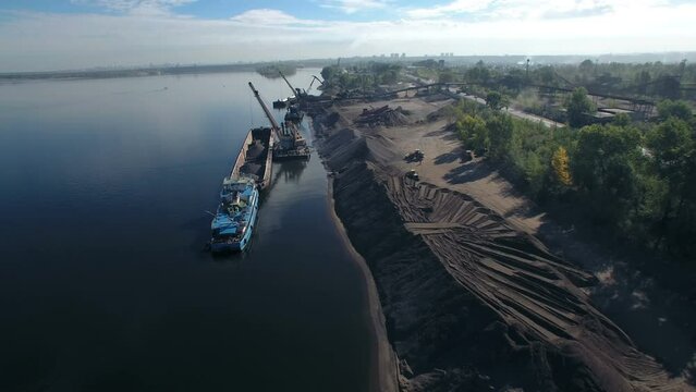 Port crane crushed stone on dry cargo ship. Morning loading of sand and crushed stone on the river in an industrial area.