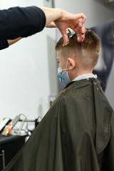 Children's haircut in the barbershop, stylish and modern haircut for schoolchildren, work during the pandemic.