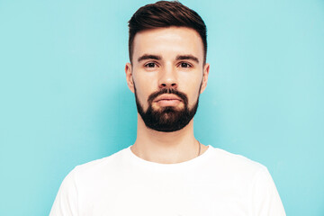 Portrait of handsome confident stylish hipster lambersexual model.Man dressed in white T-shirt and jeans. Fashion male isolated on blue wall in studio