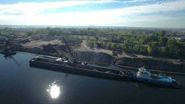 Port crane crushed stone on dry cargo ship. Morning loading of sand and crushed stone on the river in an industrial area. Aerial panorama.