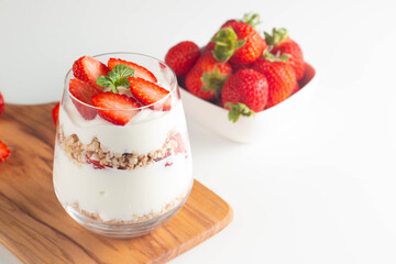 Glass with granola, yogurt and fresh strawberries on white table. Healthy breakfast bowl concept.