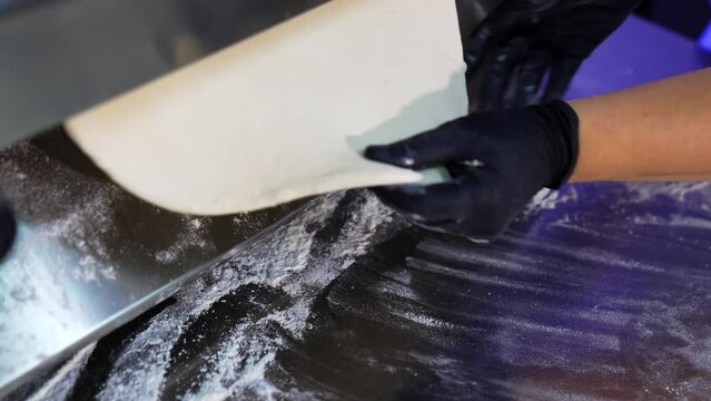 Metal roller machine for flattening dough. Gloved hands of a chef pull a flat piece of pastry from a culinary device. Close up.