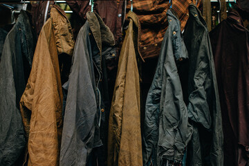 Collection of wax jackets on hangers in the shop. Many vintage men's jackets. Background and...