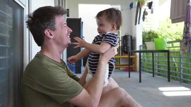 Dad and son have fun together, the kid laughs when his dad tickles him, the kid slaps his dad in the face while playing with him. Fun time for dad and baby. Father's love for son.
