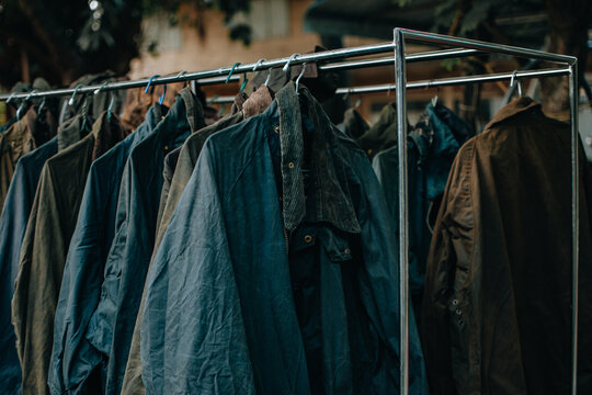 Hanger stand with vintage wax jackets. Secondhand brown jackets ,sweater and different Winter jackets. Men's wax jackets on hangers outdoors.