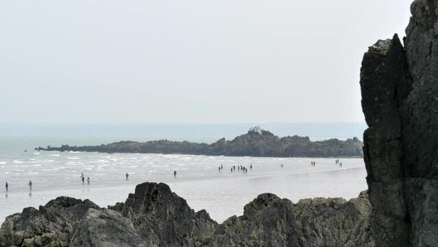 People walking along beach on cloudy day. Wind creates surf. Martin Plage, Saint-Brieuc, France.