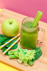 Fresh Green Smoothie of Apple, Celery, and Spinach in Glass Smoothie Jar with Yellow Cocktail Straw on Wooden Cutting Board. Vegan Detox Drink. Vegetarian Culture. Healthy Eating and Fruit Diet