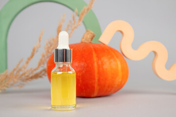 Mockup image of dropper bottle with natural organic cosmetic oil - pumpkin seed oil extract for skincare or hair with pumpkins as background. Beauty treatment, natural herbal cosmetics concept