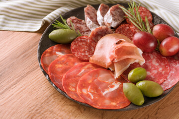 Closeup view of different meat snacks, charcuterie plate with different types of sausages - salami, bresaola, proscuitto served with olives, rosematy. Plate with italian antipasti on wooden table