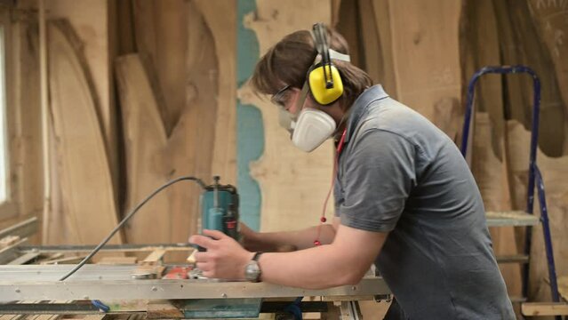 a carpenter wearing goggles, a respirator and earmuffs is processing a piece of wood