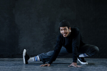 Asian hip hop young man with tattoo stretching exercise his legs on floor before dance on black...