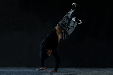 Asian young man with tattoo dancing hip hop dance stand on one hand on black background. Cool man...