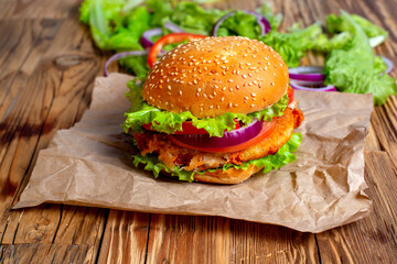 Homemade burger with cutlet, onion, tomato and salad on rustic wooden background.