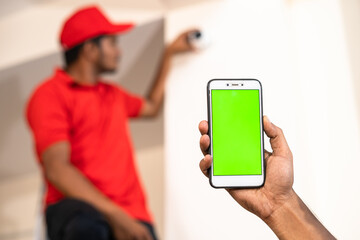 Close up shot of hands showing green screen mobile phone while while electrician fixing cctv camera at home - concept of online booking, advertisement and app promotion