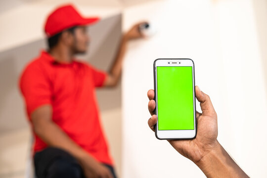 Close up shot of hands showing green screen mobile phone while while electrician fixing cctv camera at home - concept of online booking, advertisement and app promotion