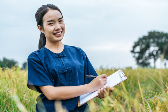 Young farmer woman writing on clipboard during work on rice field