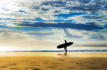 Silhouette of surfer walking along beach with surfboard