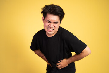 asian young man having stomachache holding his stomach with two hands on background isolated