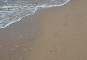 Footprints in the sand beach. Footprints in the sand against a sea wave. Footprints on a sunny day with golden sand, beach, wave and footsteps