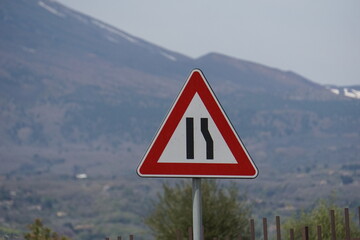 Segnale stradale strettoia asimmetrica a destra con vulcano etna sullo sfondo