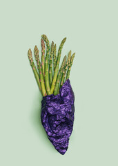 Superfood vegetarian minimal concept. Flat lay arrangement of bunch fresh organic asparagus vegetable wrapped in purple unique sheet against green background