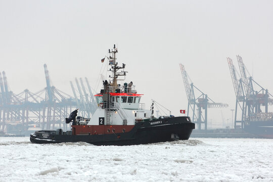 Hamburg, Germany - February 12, 2012: Tug of Hamburg in the winter and port shipyard on background.