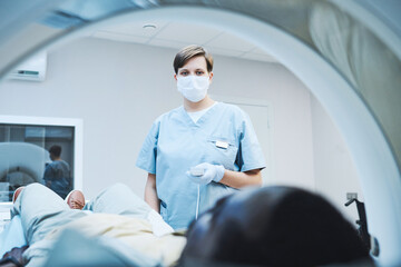 Female radiologist in mask and gloves pushing button on control panel while providing diagnostic imaging of patient