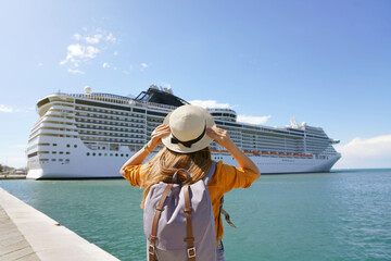 Young female backpacker holding straw hat standing in front of big cruise liner - obrazy, fototapety, plakaty