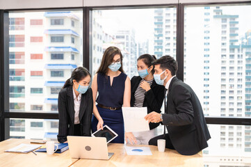 Multiethnic business team wearing face mask during business meeting in new normal office. Diverse corporate colleagues brainstorming with technology device