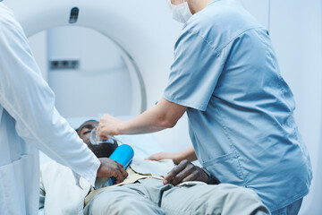 Afro-American man in serious condition getting oxygen mask from doctors while he lying on MRI table