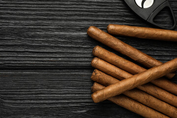 Cigars and guillotine cutter on black wooden table, flat lay. Space for text