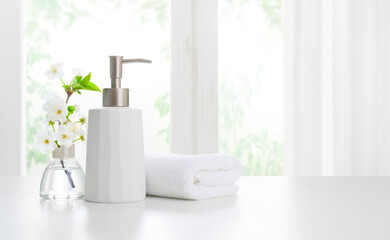 Soap dispenser with towels and aromatic flowers on light background