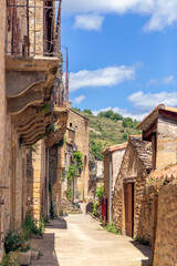 Fototapeta na wymiar Narrow light streets of Peyre village with limestone buildings of different eras with decorated balconies. Aveyron, Occitania, Southern France