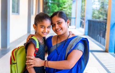 happy smiling Mother embracing her daughter before going to classrrom at school corridor by looking at camera - concept of back to school, relationship and parental love