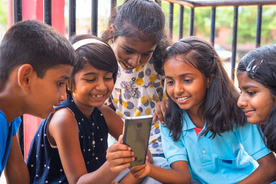 Kids At School Busy Using Mobile Phone While Sitting At Corridor During Break - Concept Of Technology, Smartphone Addiction And Using Social Media