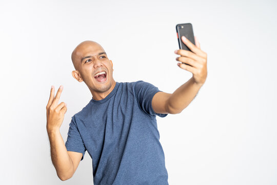 bald man with peace hand gesture selfie with phone camera on isolated background