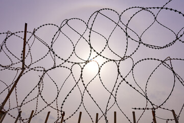 A barbed wire fence against a gloomy sky with the sun breaking through the haze.