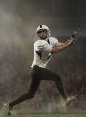 Creative portrait of young man, american football player at stadium in motion on smoked background....