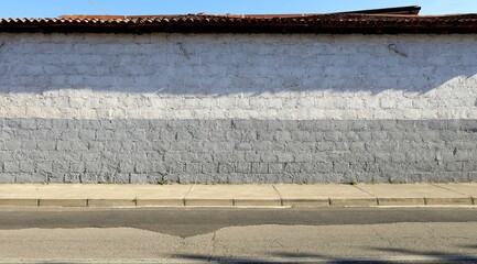 Cinder blocks wall,  painted in gray and white, with concrete sidewalk and asphalt road in front, terracotta rooftile on top. Background for copy space