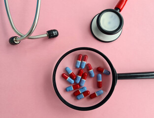 Stethoscope magnifier and medical pills on pink background