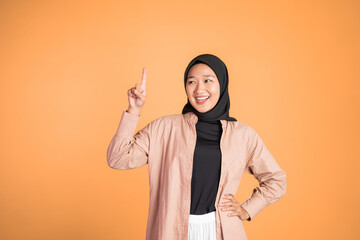 Smiling hijab woman with finger pointing up hand gesture on isolated background