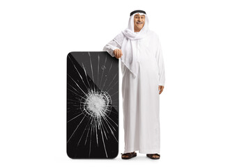 Full length portrait of an arab man in ethnic clothes leaning on a big smarphone with cracked screen