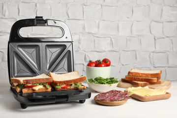 Modern grill maker with tasty sandwiches and ingredients on white wooden table - obrazy, fototapety, plakaty