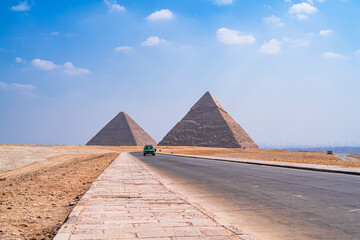 The impressive pyramids of Cheops and Kefren with the city of Cairo in the background at the foot of the road. Photograph taken in Giza, Cairo, Egypt. - obrazy, fototapety, plakaty