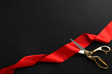 Red ribbon and scissors on black background, top view. Space for text