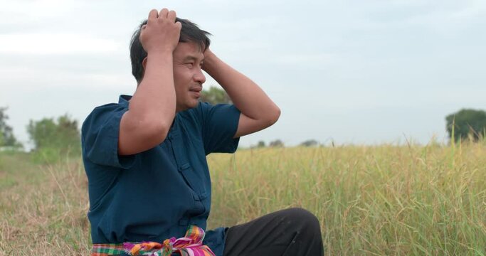 Portrait shot of Tired Asian farmer man in a blue dress holding hands massages forehead and head with severe pain in the paddy field.