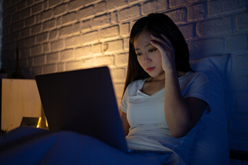 Exhausted Young business woman using laptop working late at night on bed