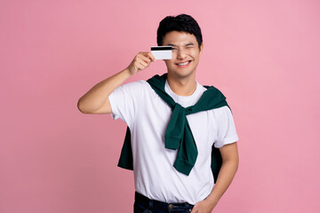 Smiling handsome young man in casual clothes posing alone on a pink wall photo studio background. He holds a bank card