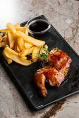 Grilled quail carcass with french fries on plate over black stone background. Roasted quails on plate. Top view, flat lay